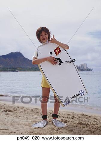 Stock Image - Young woman at a beach, holding paddleboard . Fotosearch