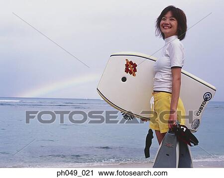 Young woman at a beach, holding paddleboard and flippers View Large Photo Image Stock Image - Young woman at a beach, holding paddleboard and flippers. Fotosearch