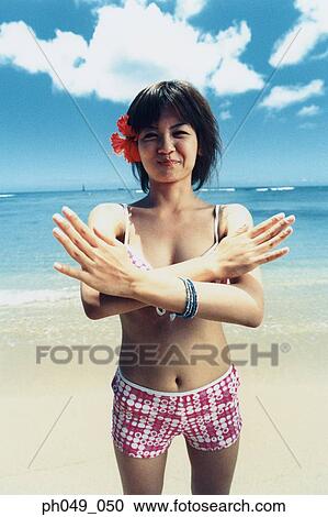 Stock Image - Young woman in bikini at a beach, arms crossed, portrait. Fotosearch