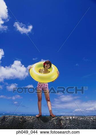 Picture - Young woman in bikini at a water breaker, holding yellow float. Fotosearch