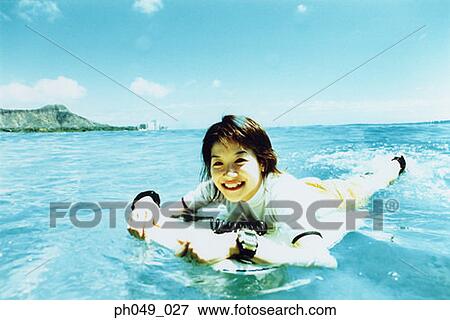 Stock Photo - Young woman lying on paddleboard in ocean. Fotosearch