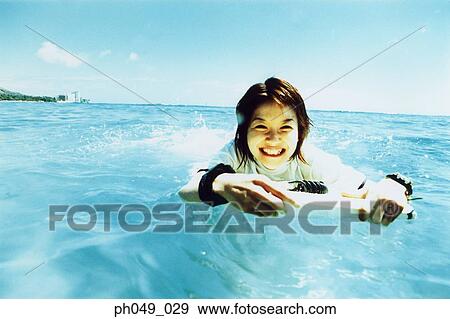 Stock Photo - Young woman lying on paddleboard in ocean. Fotosearch