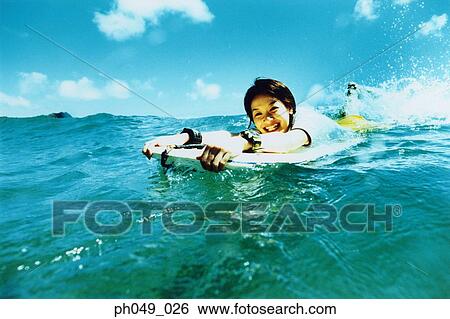 Stock Photograph - Young woman lying on paddleboard in ocean. Fotosearch