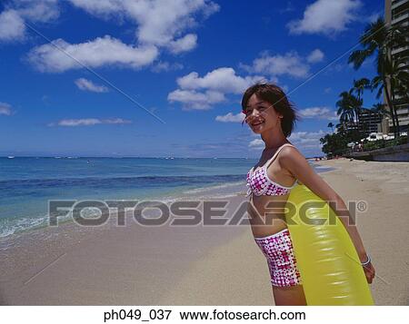 Stock Photo - Young woman on beach holding yellow float. Fotosearch