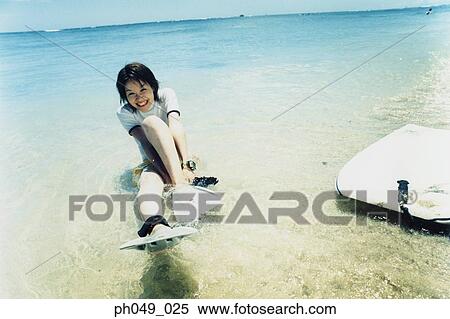 Stock Photography - Young woman putting on flippers on beach. Fotosearch