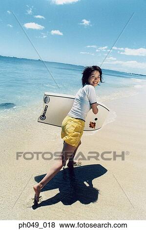 Stock Photo - Young woman running at a beach with surfboard . Fotosearch