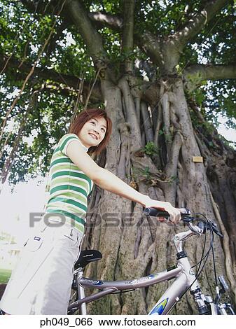 Stock Photograph - Young woman sitting on bicycle, low angle view. Fotosearch