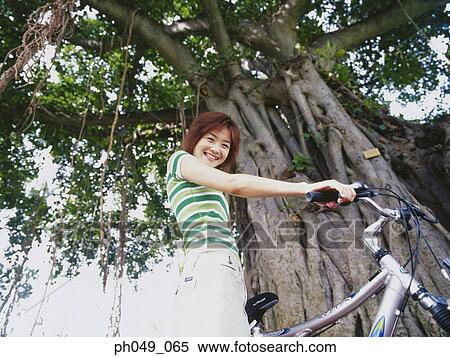 Young woman sitting on bicycle, low angle view View Large Photo Image Stock Photography - Young woman sitting on bicycle, low angle view. Fotosearch