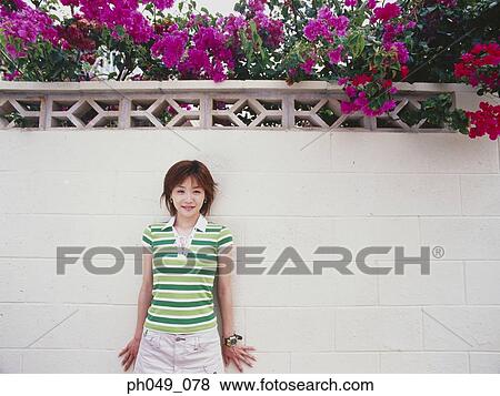 Stock Photo - Young woman standing against wall. Fotosearch