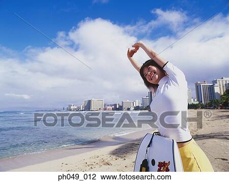Stock Image - Young woman stretching on beach, paddleboard leaning on her body. Fotosearch