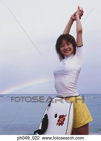 Stock Image - Young woman stretching on beach, paddleboard leaning on her body. Fotosearch
