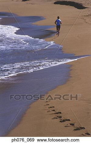 Stock Photo - Man jogging along a beach, rear view. Fotosearch