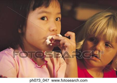 Young Asian girl eating creamy cake, Caucasian girl watching View Large Photo Image Stock Photo - Young Asian girl eating creamy cake, Caucasian girl watching. Fotosearch