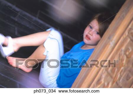 Picture - Young girl sitting behind door, taking off shoes. Fotosearch