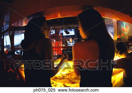Stock Photography - Two young women sitting at bar table, rear view. Fotosearch