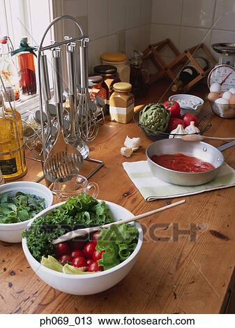 Stock Image - Bowl of salad and ingredients on kitchen table. Fotosearch