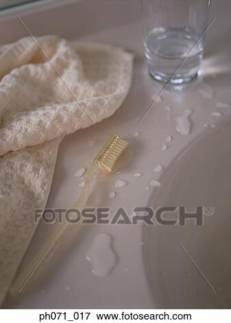 Stock Photo - Towel, glass of water and toothbrush on bathroom sink, close-up. Fotosearch