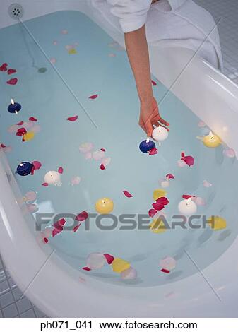 Stock Image - Woman putting candles and petals in bathtub of water. Fotosearch