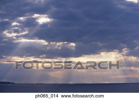 Setting sun shining through clouds over ocean View Large Photo Image Picture - Setting sun shining through clouds over ocean . Fotosearch