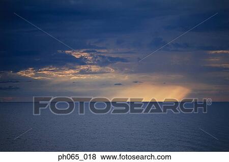 Setting sun shining through dark clouds over ocean View Large Photo Image Stock Photo - Setting sun shining through dark clouds over ocean . Fotosearch