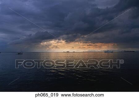 Setting sun shining through dark clouds over ocean View Large Photo Image Stock Photo - Setting sun shining through dark clouds over ocean . Fotosearch