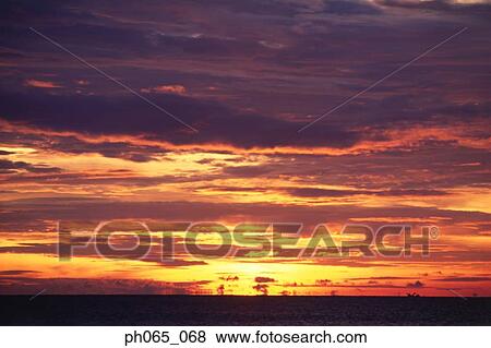 Stock Photo - Sunset at sea, dark clouds in orange streaked sky . Fotosearch