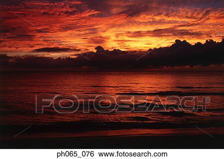 Sunset at sea, dark clouds in orange streaked sky View Large Photo Image Stock Photograph - Sunset at sea, dark clouds in orange streaked sky . Fotosearch