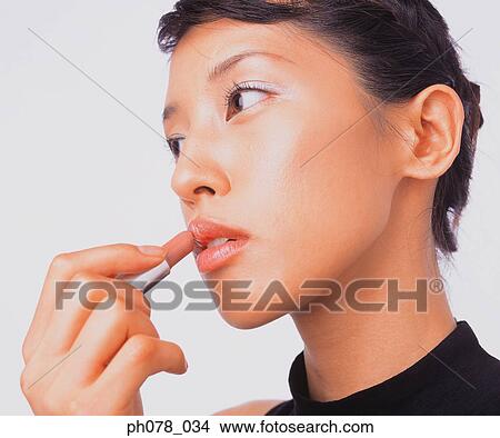 Picture - Young woman applying lipstick. Fotosearch