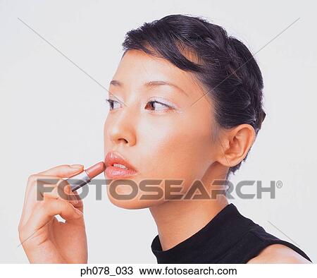 Stock Image - Young woman applying lipstick. Fotosearch
