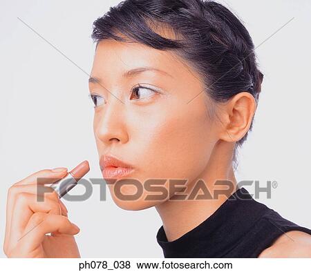 Stock Photo - Young woman applying lipstick. Fotosearch