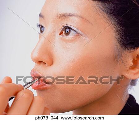 Young woman applying lipstick with a lip brush View Large Photo Image Picture - Young woman applying lipstick with a lip brush. Fotosearch
