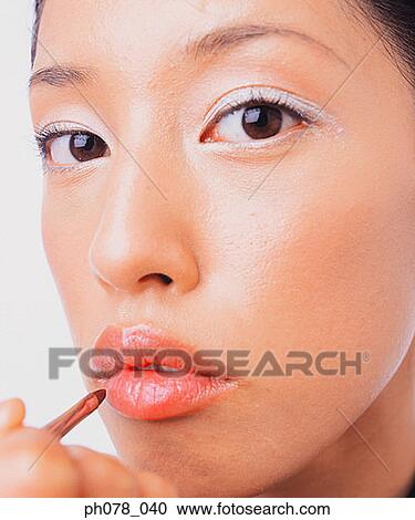 Stock Image - Young woman applying lipstick with a lip brush. Fotosearch