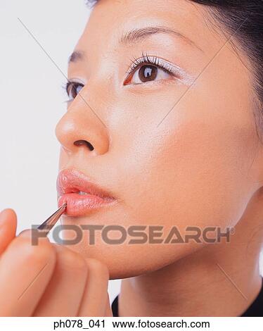 Stock Image - Young woman applying lipstick with a lip brush. Fotosearch