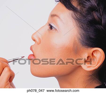 Young woman applying lipstick with a lip brush View Large Photo Image Stock Photo - Young woman applying lipstick with a lip brush. Fotosearch