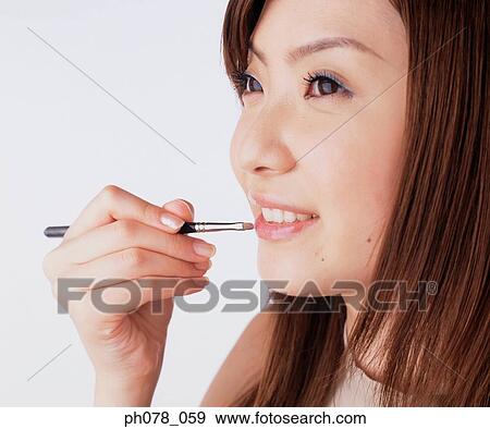 Young woman applying lipstick with a lip brush View Large Photo Image Stock Photo - Young woman applying lipstick with a lip brush. Fotosearch