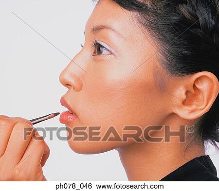 Stock Photograph - Young woman applying lipstick with a lip brush. Fotosearch