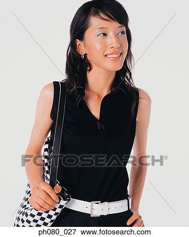 Stock Photo - Young woman carrying handbag, hand on hip. Fotosearch