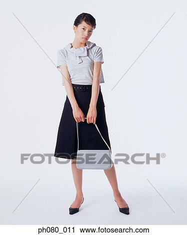 Stock Image - Young woman holding handbag, posing. Fotosearch