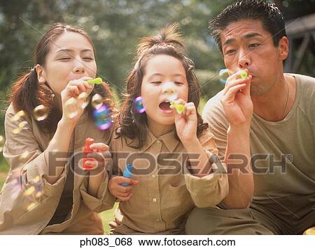 Stock Photo - Family of three blowing soap bubbles. Fotosearch