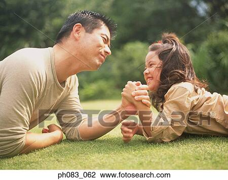Stock Image - Father arm-wrestling with daughter on lawn. Fotosearch