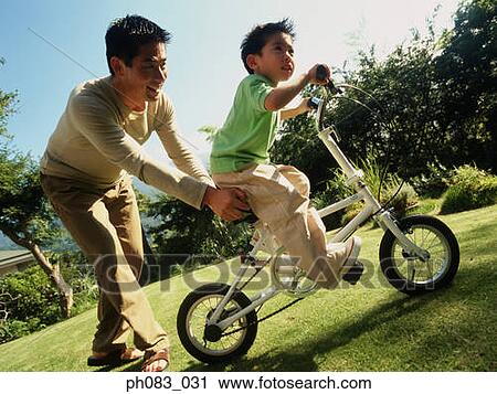 Stock Image - Father teaching young son to ride bicycle . Fotosearch