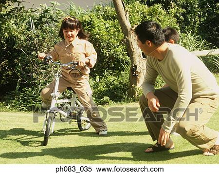 Young daughter riding bicycle, father keeping watch on her View Large Photo Image Stock Photography - Young daughter riding bicycle, father keeping watch on her. Fotosearch