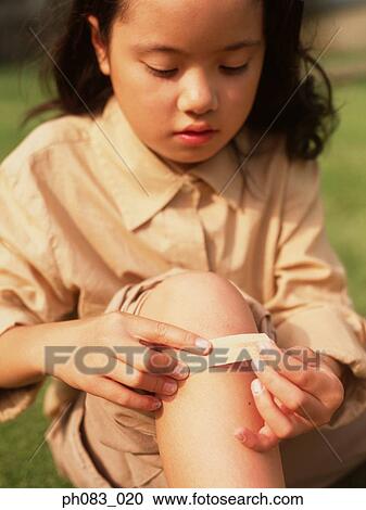Stock Image - Young girl applying plaster on knee. Fotosearch