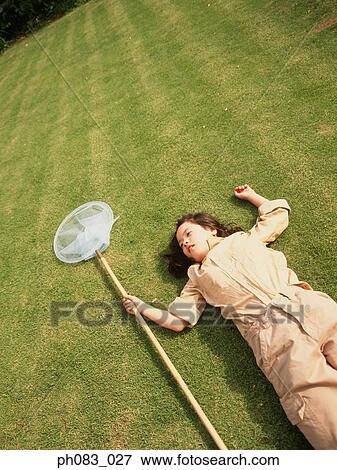 Young girl lying on grass holding a butterfly net View Large Photo Image Stock Photo - Young girl lying on grass holding a butterfly net. Fotosearch