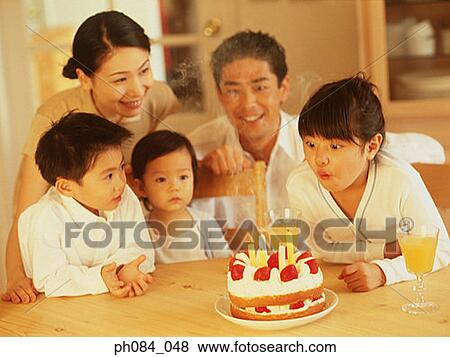 Stock Photo - Family celebrating daughter's birthday, daughter blowing cake. Fotosearch