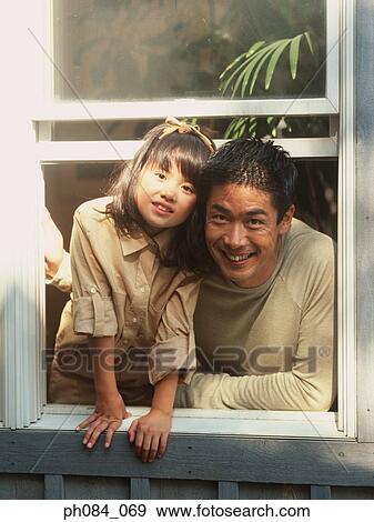 Stock Photo - Father and daughter leaning out of window, smiling. Fotosearch