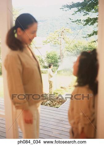 Picture - Mother and daughter, father spraying water in the garden. Fotosearch