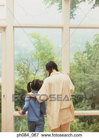 Stock Photo - Mother and daughter standing by window. Fotosearch