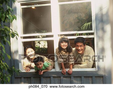 Stock Image - Whole family leaning out of window, smiling. Fotosearch