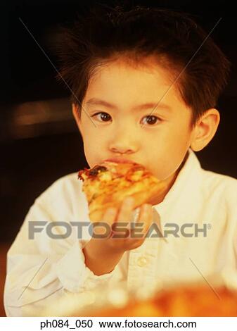 Stock Image - Young boy eating slice of pizza, close-up . Fotosearch